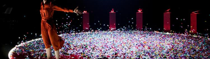 Performer on stage covered with confetti, spreading her arms wide open and looking up 
