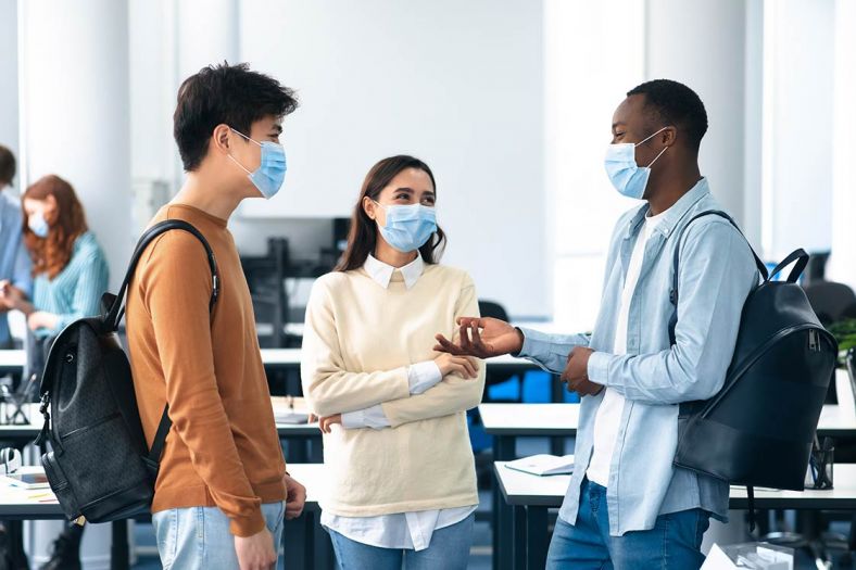 Three adults in surgical masks have a conversation in a classroom