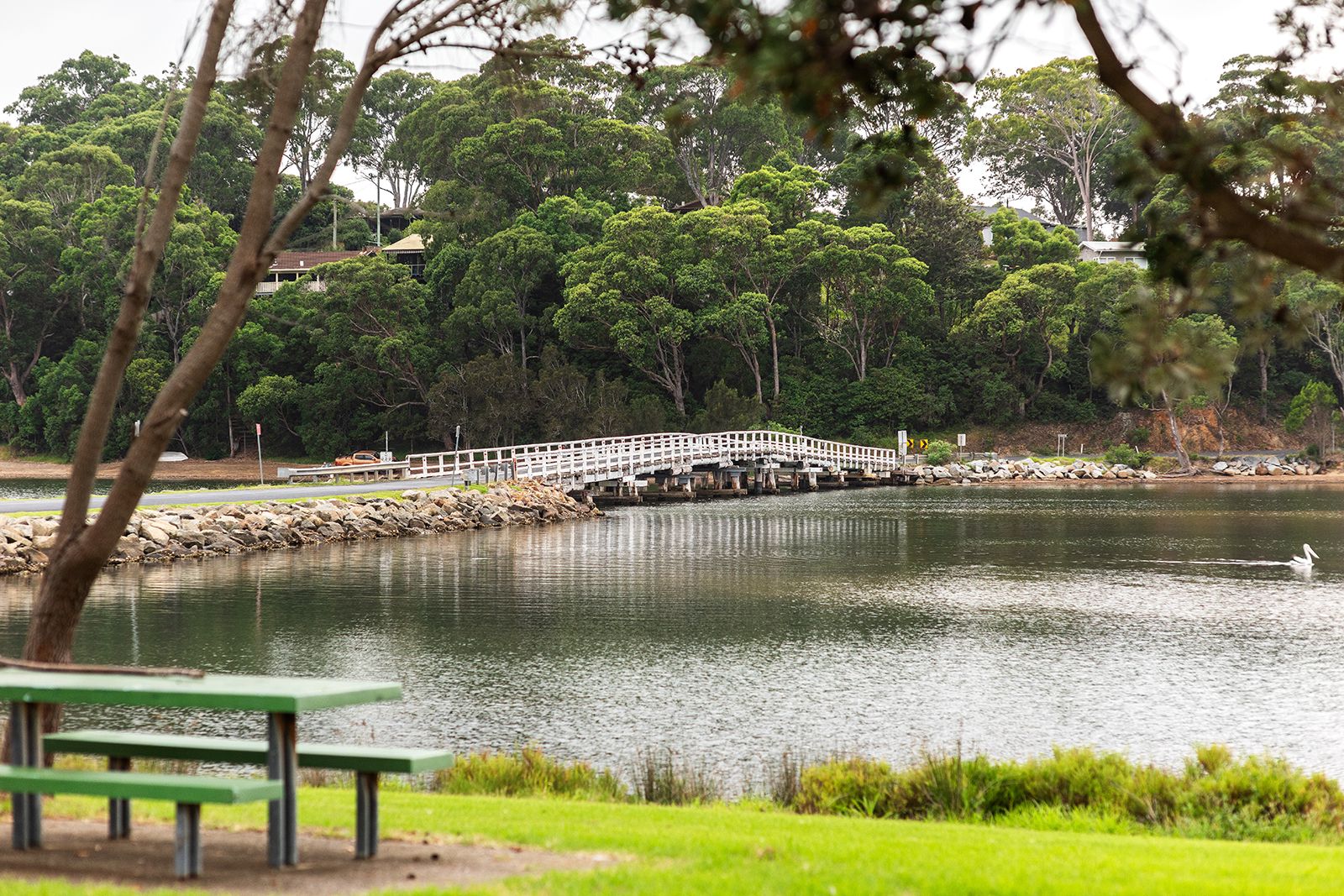 Wallaga lake bridge on still cloudy day with picnic bench in foreground