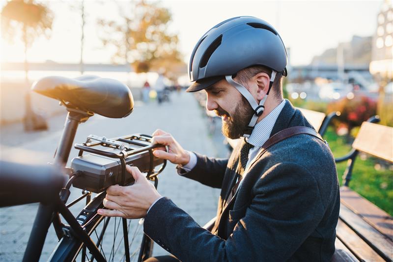 An e-bike with cyclist next to it, adjusting the power pack at the back of the e-bike