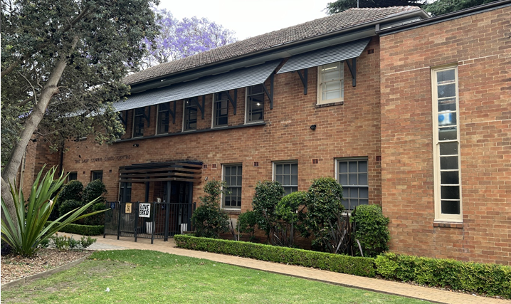 A two-storey brick building surrounded by trees and shrubs