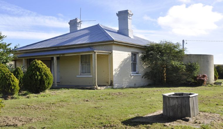 A front on view of a historical house painted cream with a chimney