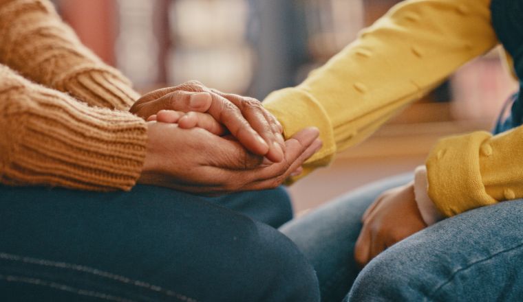 Two women sitting facing each other wearing jeans and jumpers