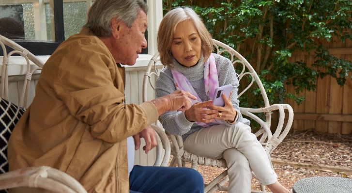 A senior couple sitting outside looking at a mobile phone