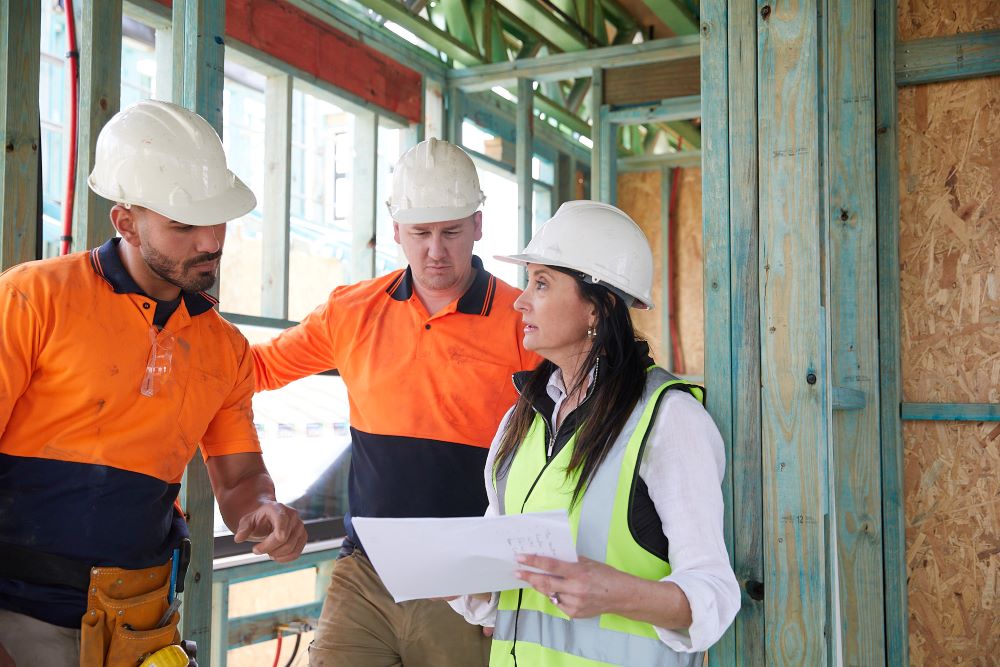 A female building inspector speaking to two tradies at a building site.