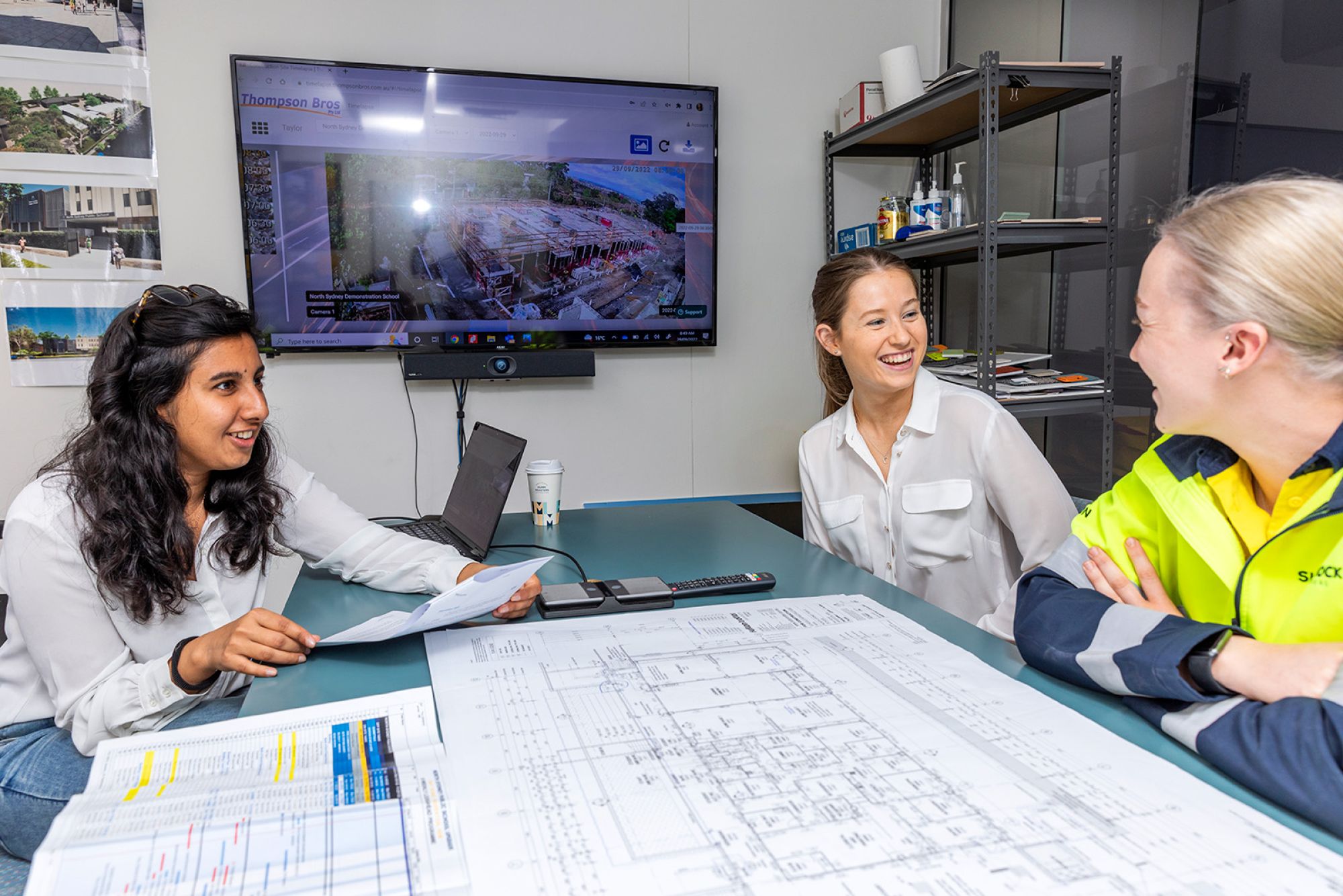 Three people read building plans in an office.