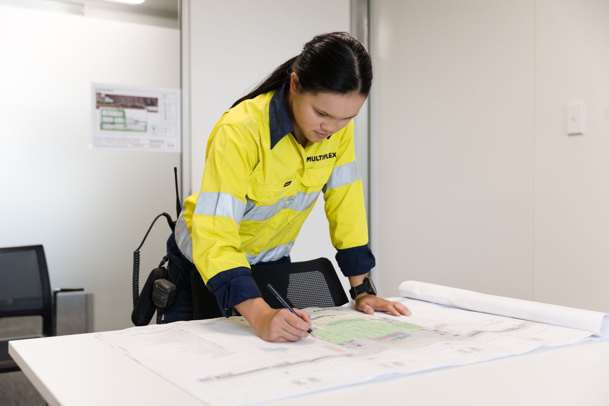 Kaitlyn marks up a site blueprint in a construction office.