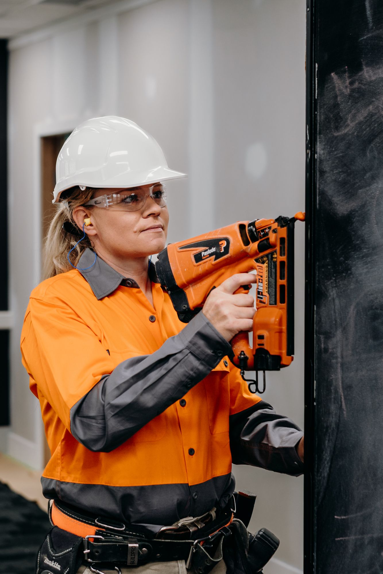 Annie in a hard hat using powder a actuated tool.