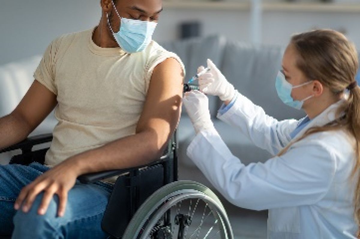 A doctor in a mask giving a man in a wheelchair, who is also wearing a mask, a vaccine.