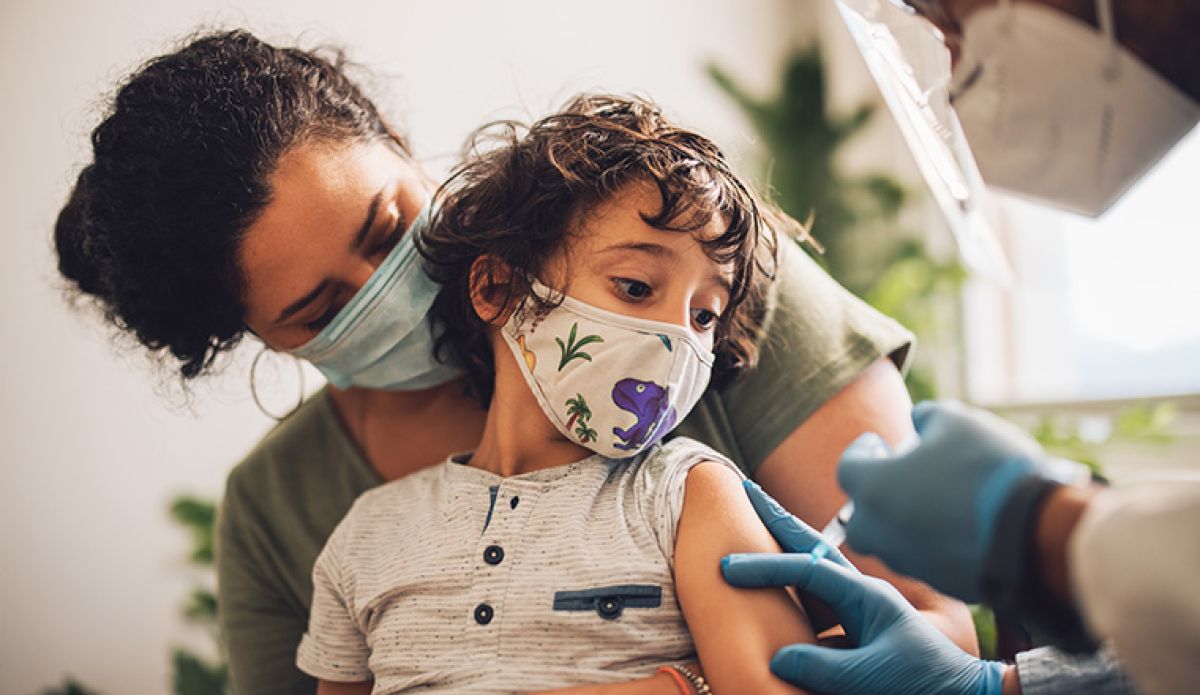 A child sit on his mother's lap whilst a masked doctor is administering a vaccine