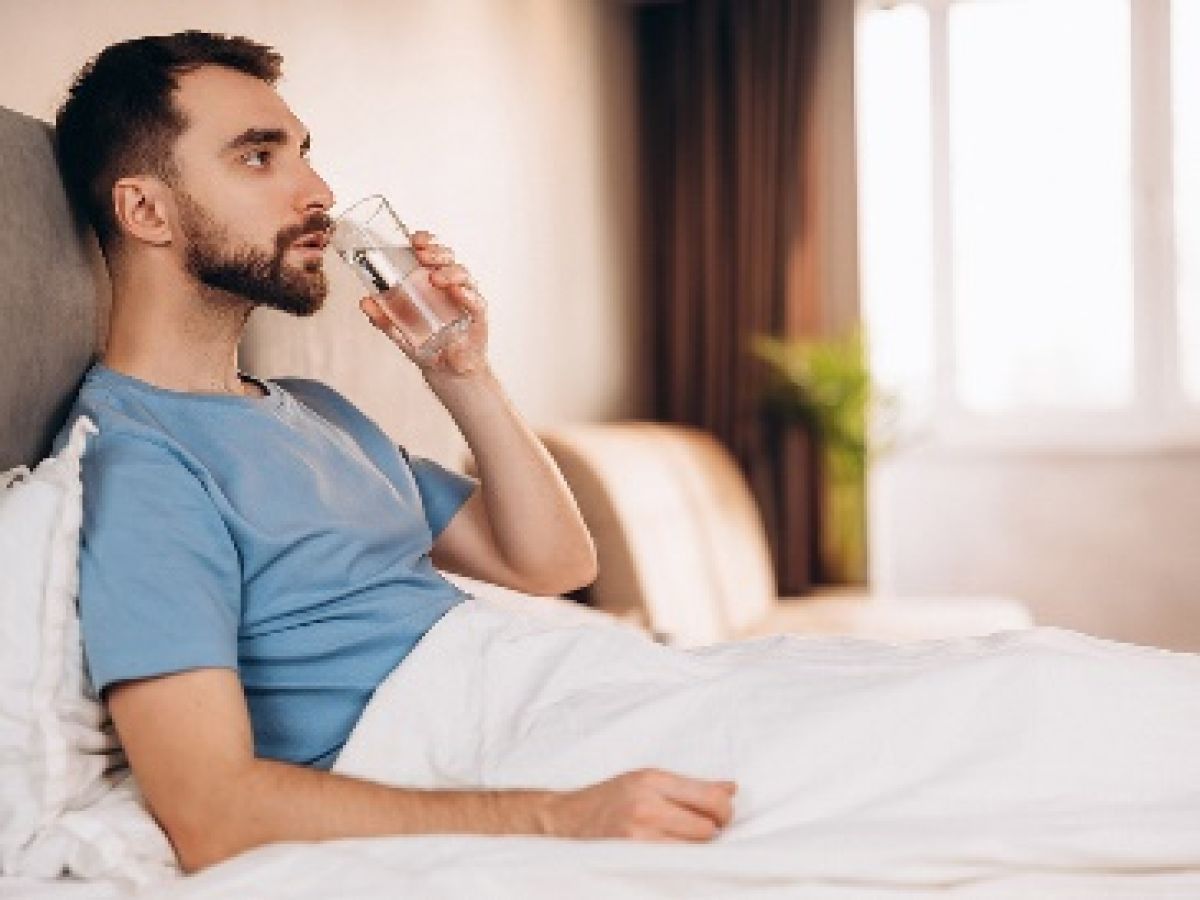 man-laying-in-bed-sips-water