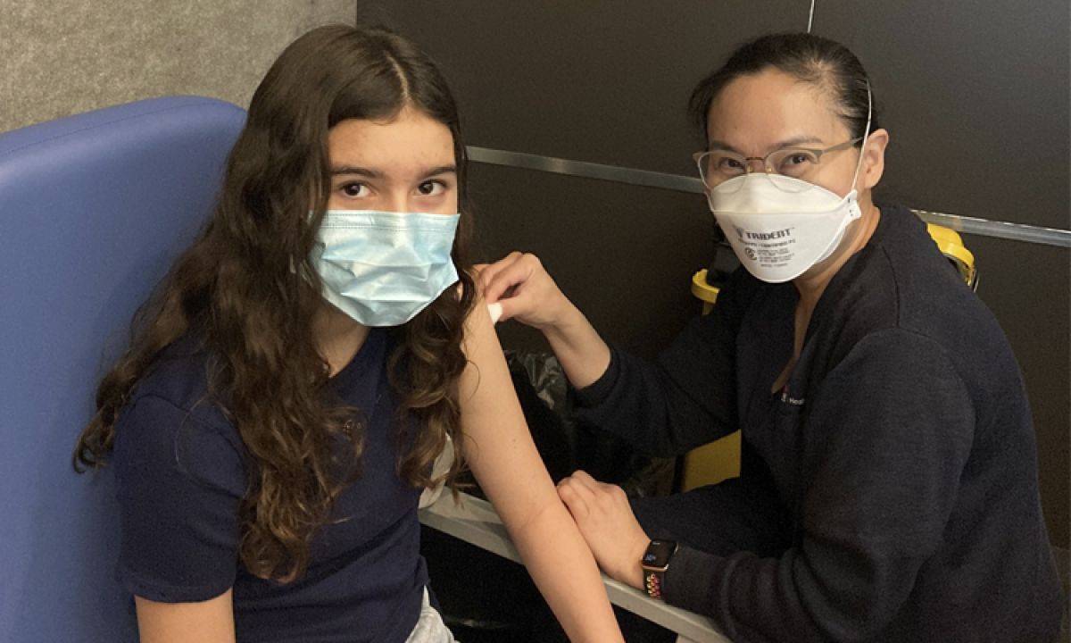 Young woman wearing mask gets needle in arm from a staff member