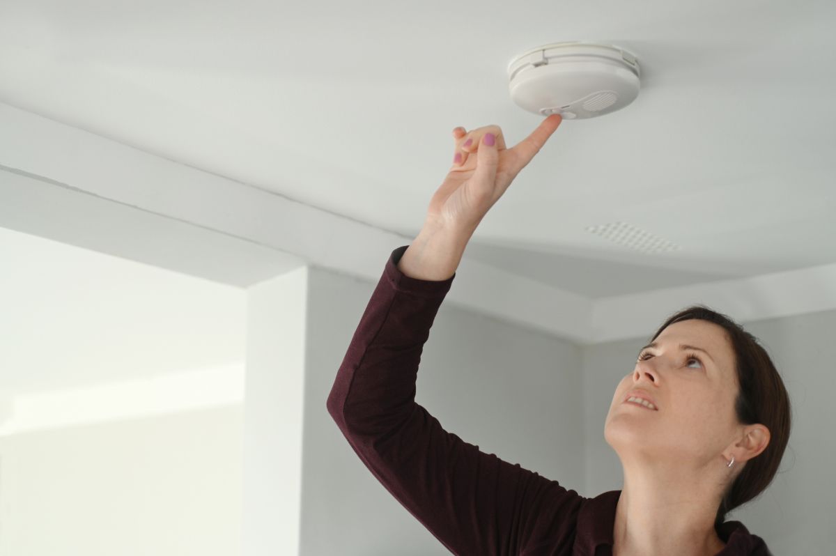Woman pressing button on ceiling smoke alarm.