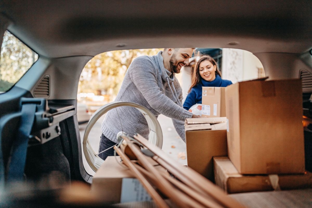 Couple packing car boot with furniture such as a lamp and boxes.