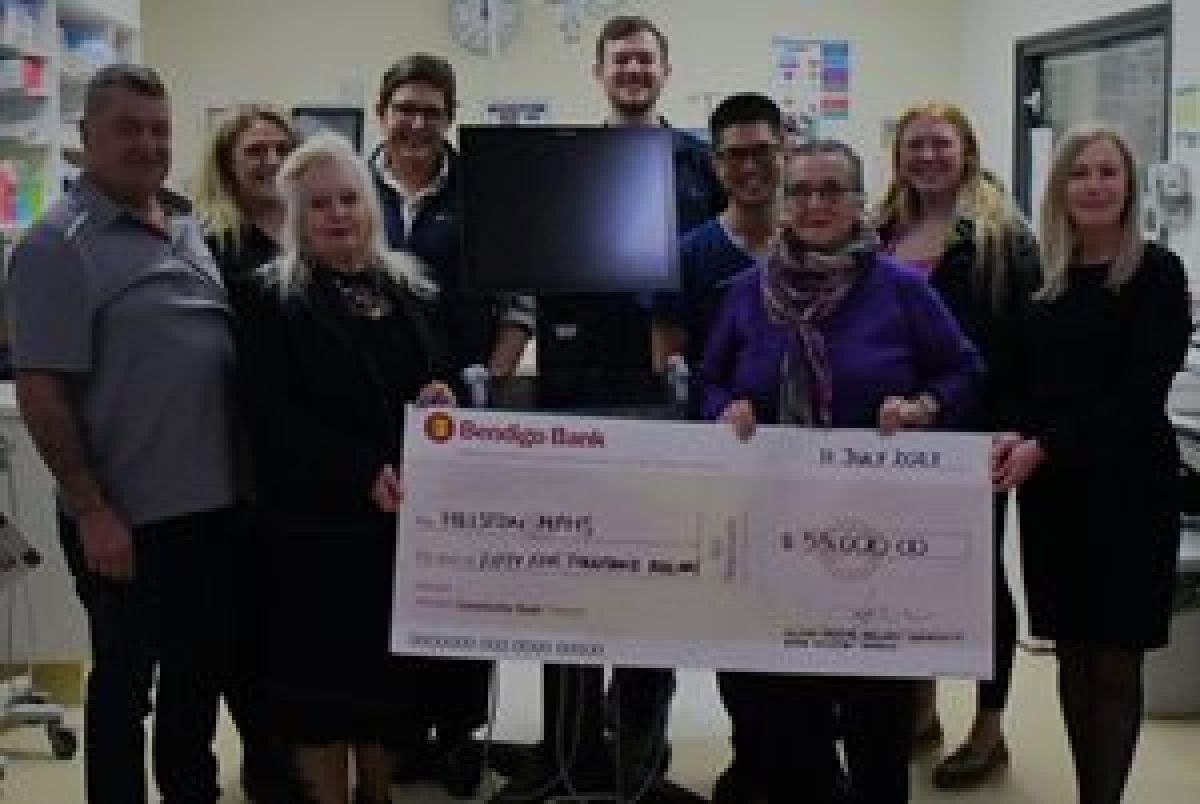 Staff from the Hillston multipurpose service stand around a newly donated ultrasound machine inside the facility. Some of the staff are holding up a large commemorative donation cheque from Bendigo Bank with the amount $55,000 written on it.