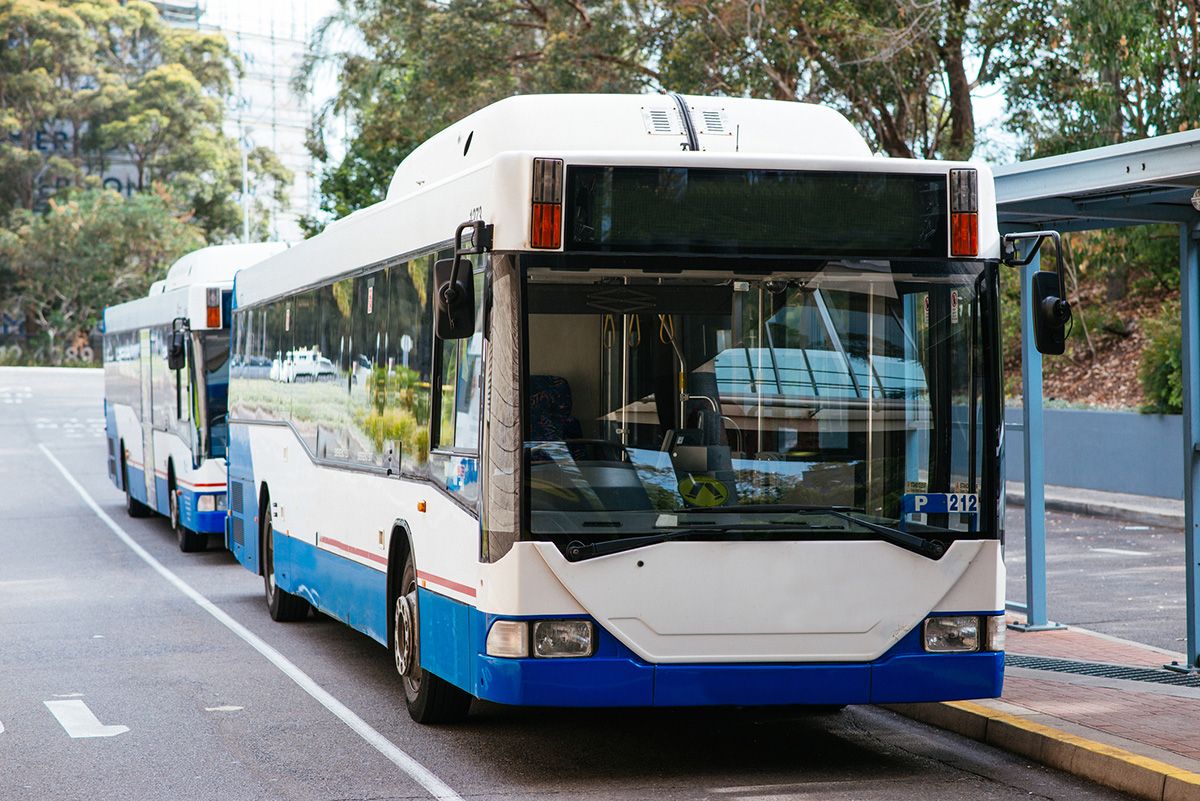 2 buses stationed at a bus stop in NSW. It is a clear day and there are no people at the stop.