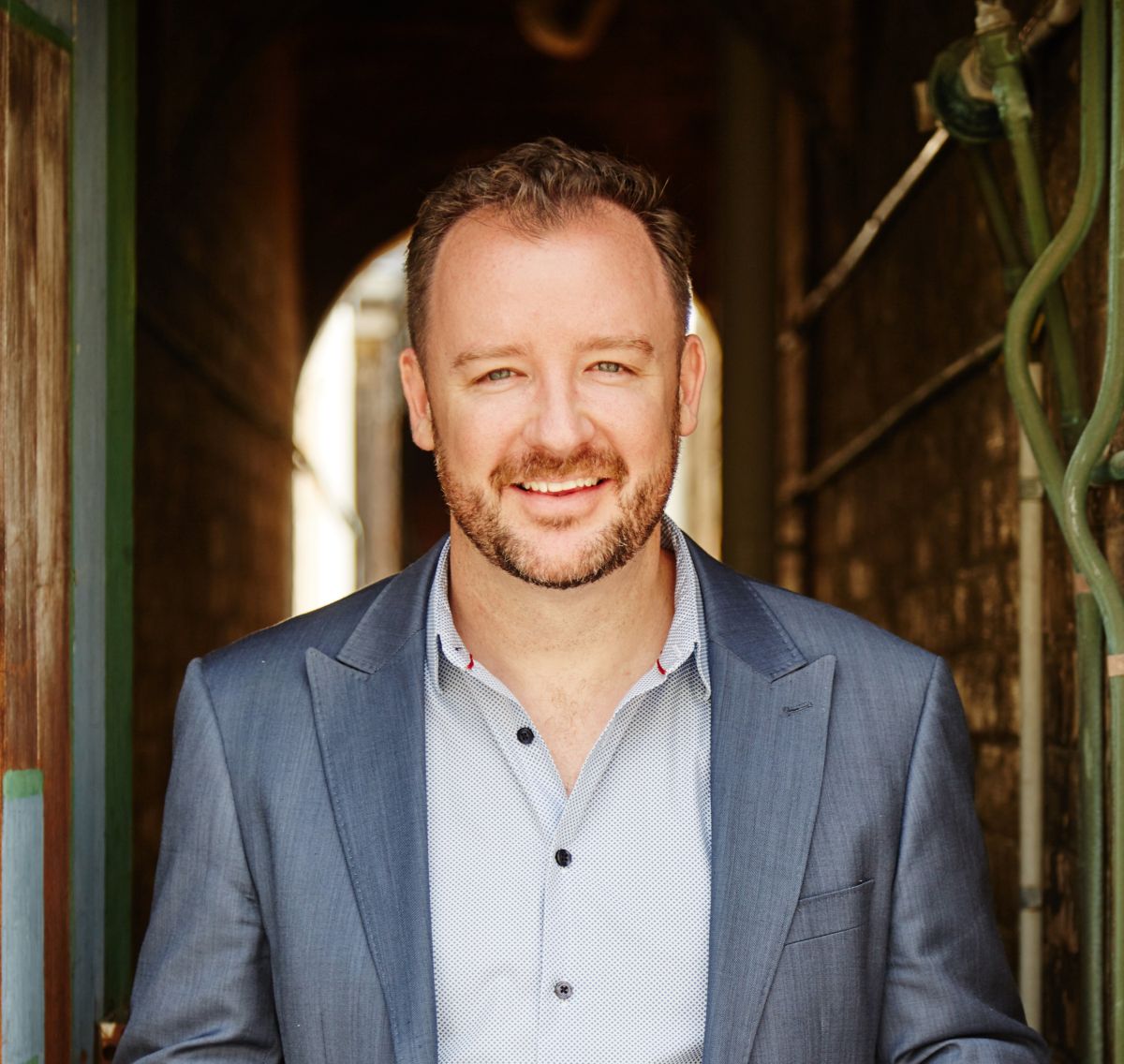 A man is looking at the camera and smiling. He is wearing a shirt and jacket. 