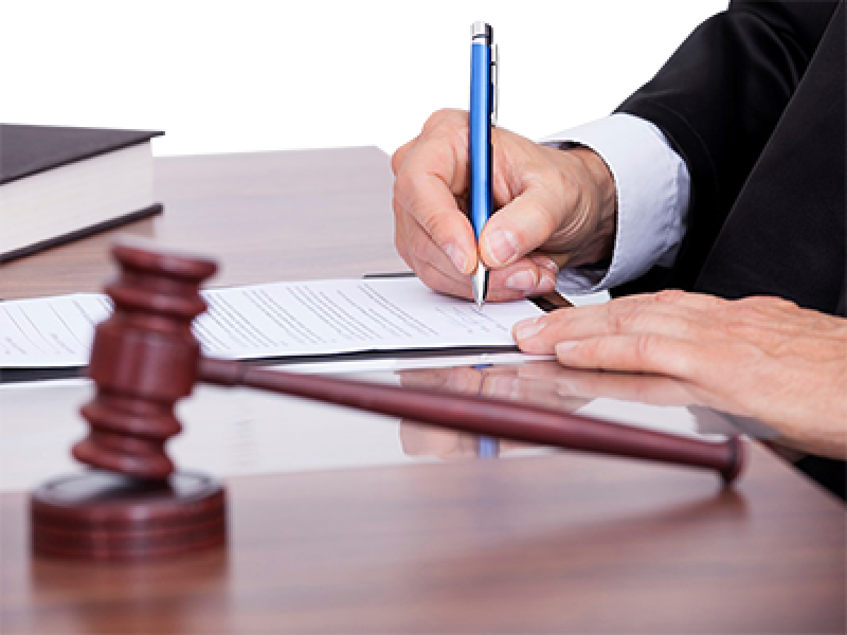 A judge writing on a document next to a gavel in a court.