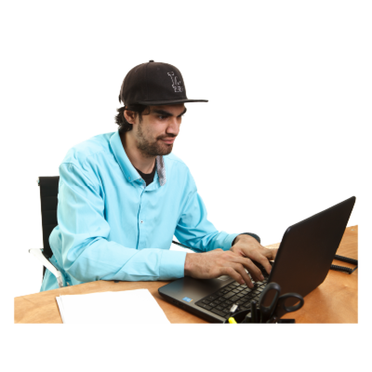 A man in a baseball cap uses a laptop at a desk.