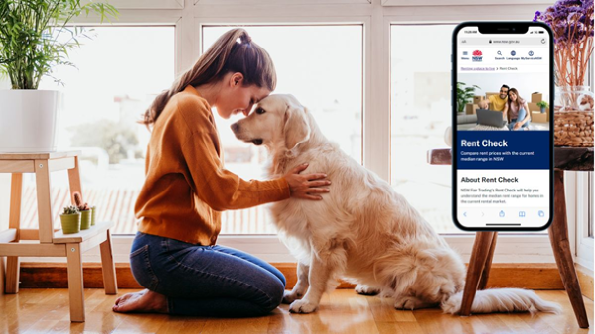 A woman kneels on a wooden floor, gently resting her forehead against her golden retriever’s head in a moment of connection. Natural light streams through large windows, brightening the room. To the right, a smartphone screen displays the "Rent Check" page from the NSW Government website.