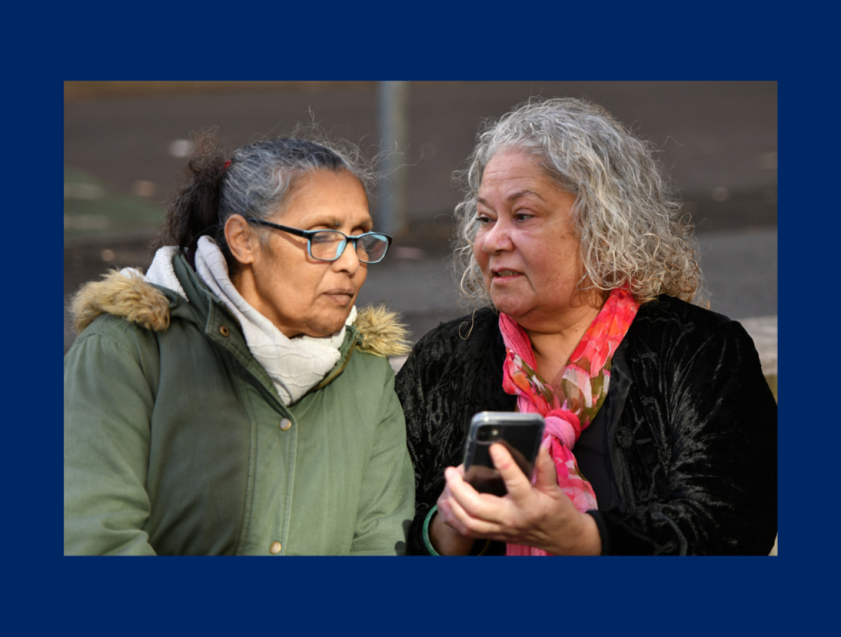 two women stand and talk while holding a phone