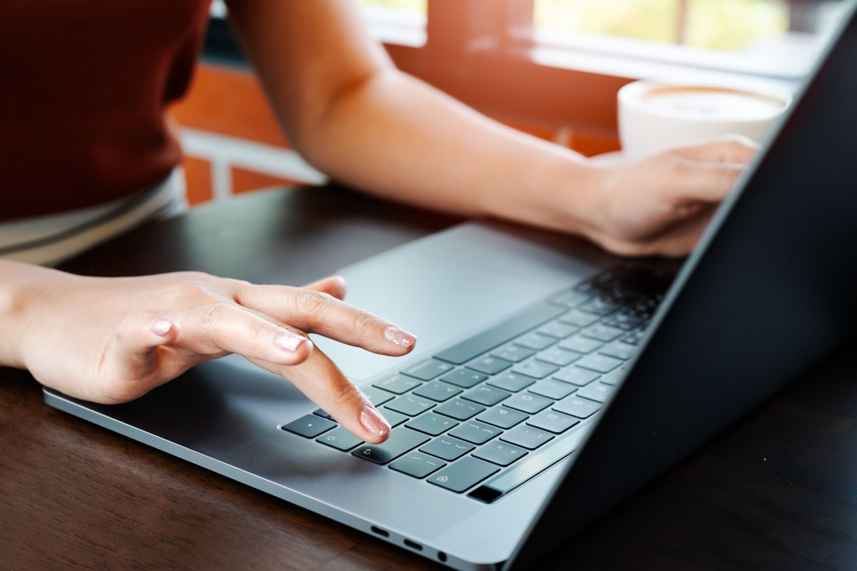 Two well-manicured hands on a laptop with a cup of coffee in the background.