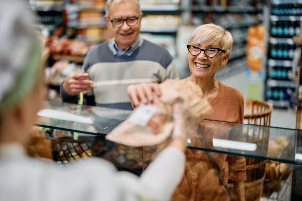 Two seniors smiling getting handed purchased items over a counter