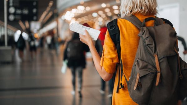 A woman in an orange jumper walks through an airport with tickets