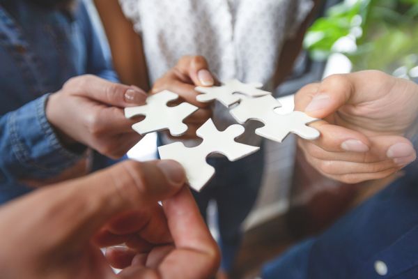 Close-up of many people hands holding a jigsaw puzzle piece in circle together.