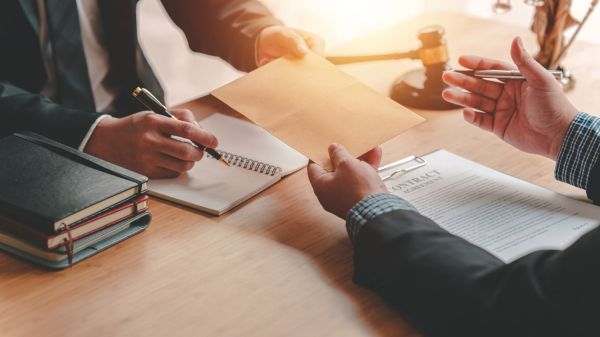 Two men at a desk discuss and sign legal documents