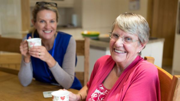 A young woman has a cup of tea with an older woman as a volunteer