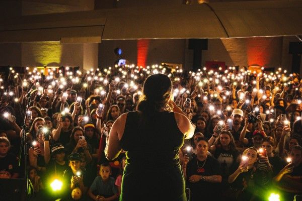 Silhouette of a singer on stage looking out towards the crowd who are holding their phone torches up.