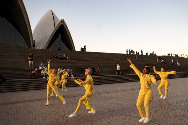 A group of dancers in yello tracksuits dancing on the stairs of the Opera House