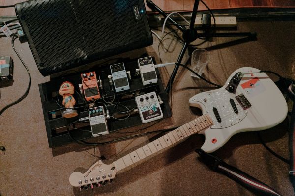 An electric guitar lying on the ground next to a case of sound equipment.