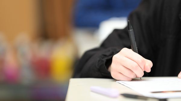 Close up of hand holding pen in exam with exam paper on a table.