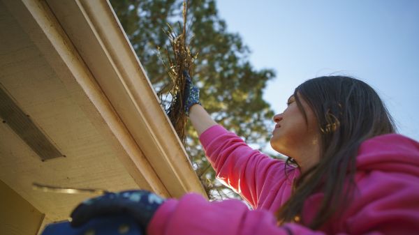 Woman wearing gloves cleaning gutters on a roof