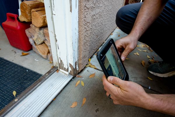 Kneeling person holding phone camera in front of worn white painted door frame.