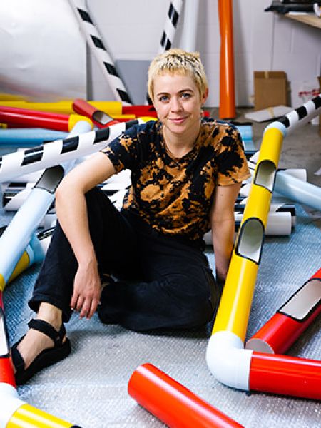 Parramatta artist Nadia Odlum is seated amidst a collection of colourful plastic pipes.