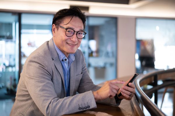 A man with glasses uses a mobile phone against a railing.