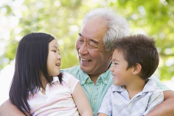 A grandparent with their arms around two children, one on each side. They all look at each other, smiling.