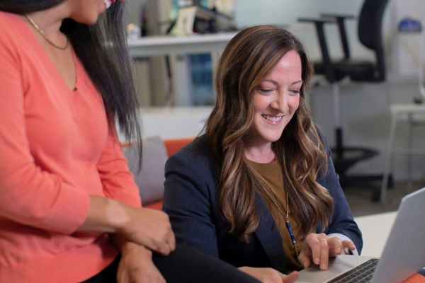 A woman using a laptop as a colleague watches on.