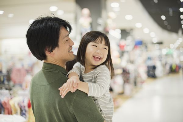 A smiling man holding a smiling young child inside a shopping centre. 