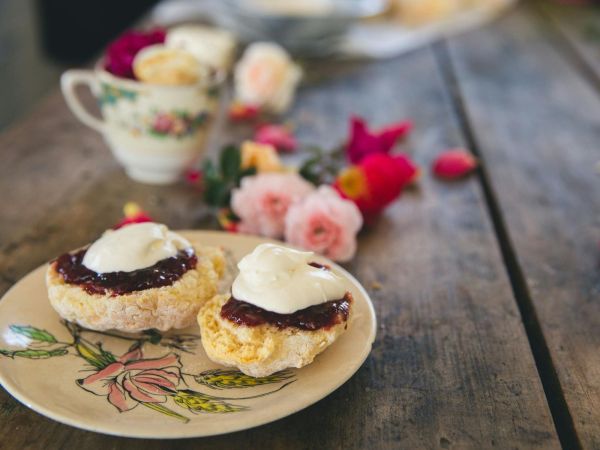 Plate of scones with jam and cream. Flowers and tea in the background.