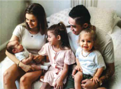 Aboriginal woman Keely-Jai smiling down at her newborn, with her partner and young daughters as well