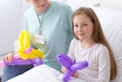 Volunteer giving balloons to a sick girl in a hospital bed