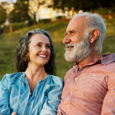 Woman in blue shirt with man in light orange shirt smiling outdoors in golden light.