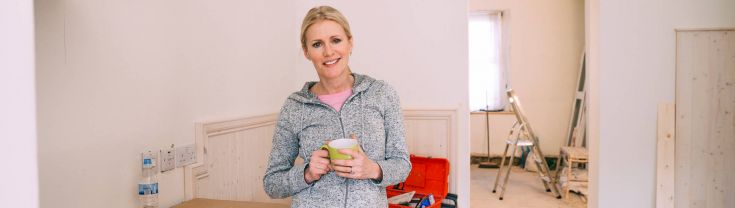 A woman stands with a cup in her hand smiling in a house that is being renovated