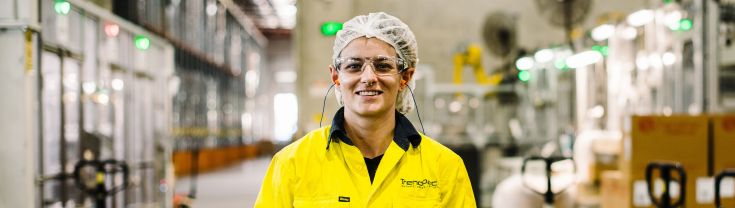 Image of a young man in a food processing facility wearing a hair net and smiling