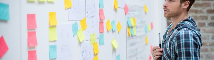 Man using a whiteboard with post-it notes and tablet