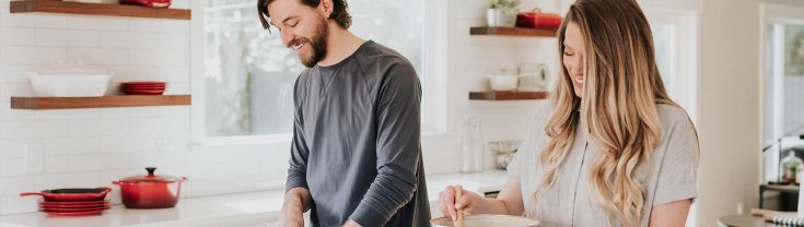 A man and woman are cooking with pots on a stove in a kitchen